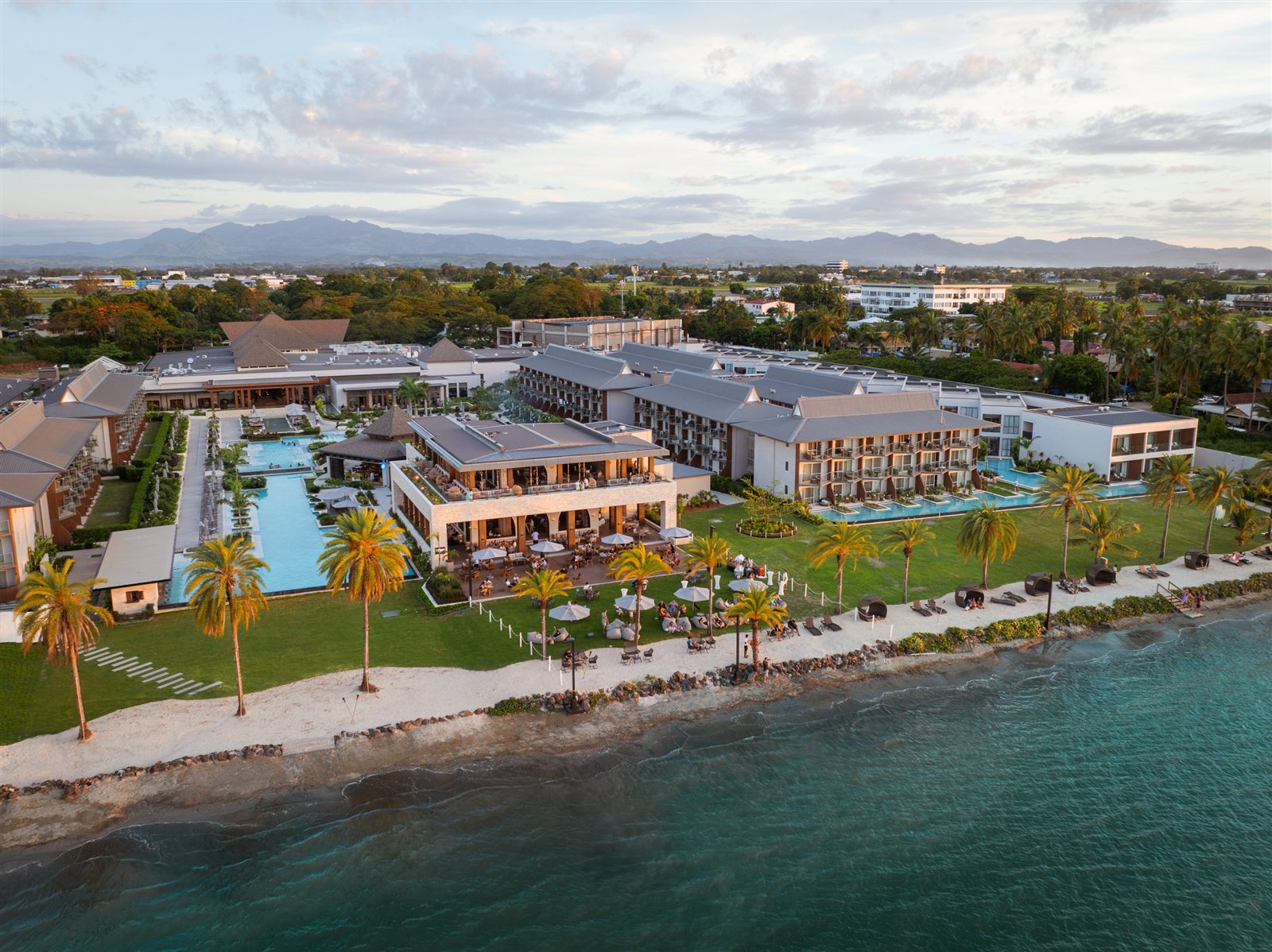 Aerial view of the Crowne Plaza Fiji Nadi Bay Resort at dusk, showing pools, restaurants, palm-lined lawns, and the shoreline.